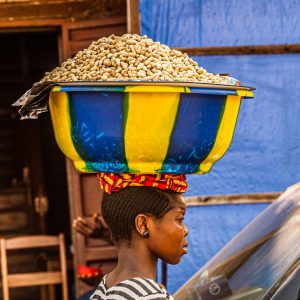 African saleswoman carries a bowl of peanuts on her head