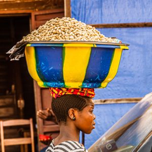 African woman carries bowl of peanuts on her head